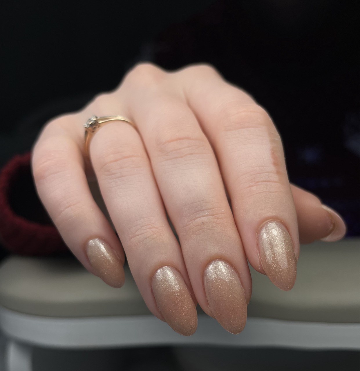 Hand met champagnekleurige glitternagels in amandelvorm en een ring