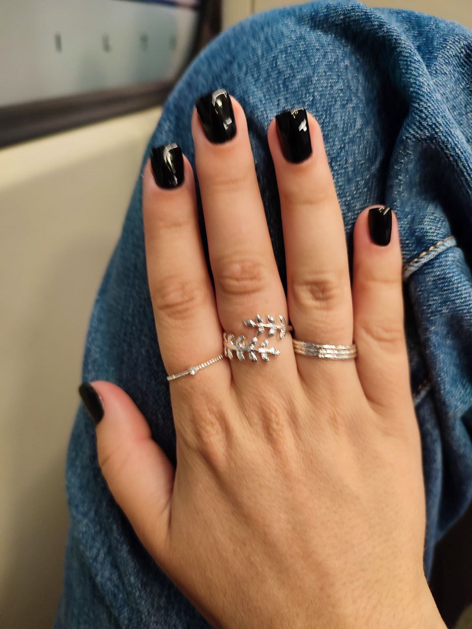Hand met zwarte nagels en zilveren ringen tegen een spijkerjas