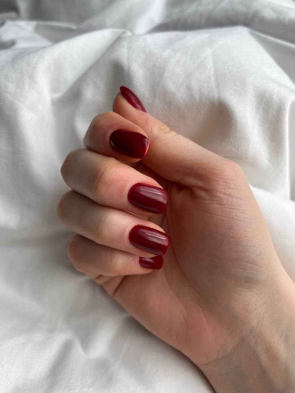 Hand met diep donkerrode gelakte nagels op wit beddengoed