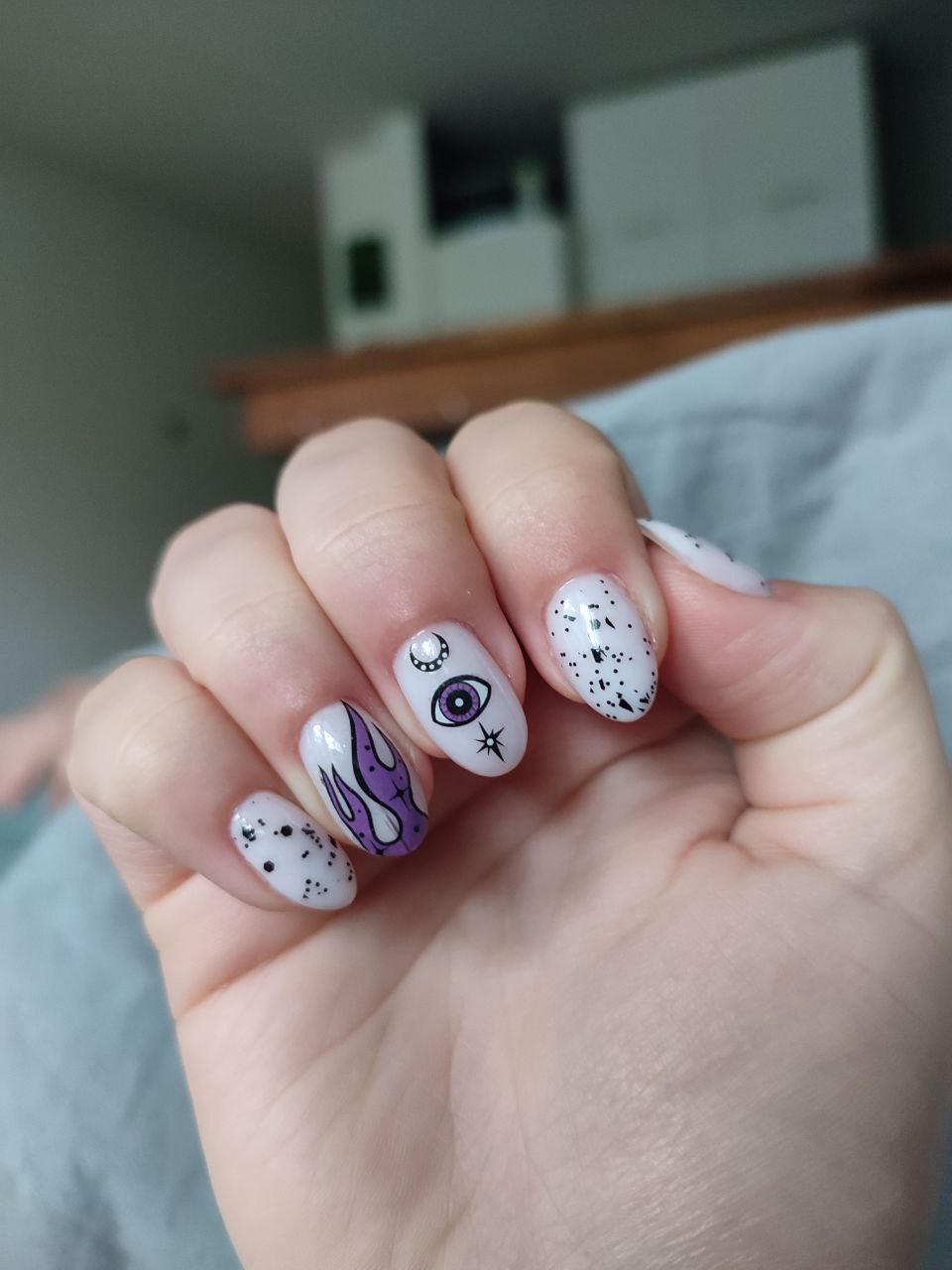 Witte nagels met zwarte nail art: een oog, vlammen en sterretjes